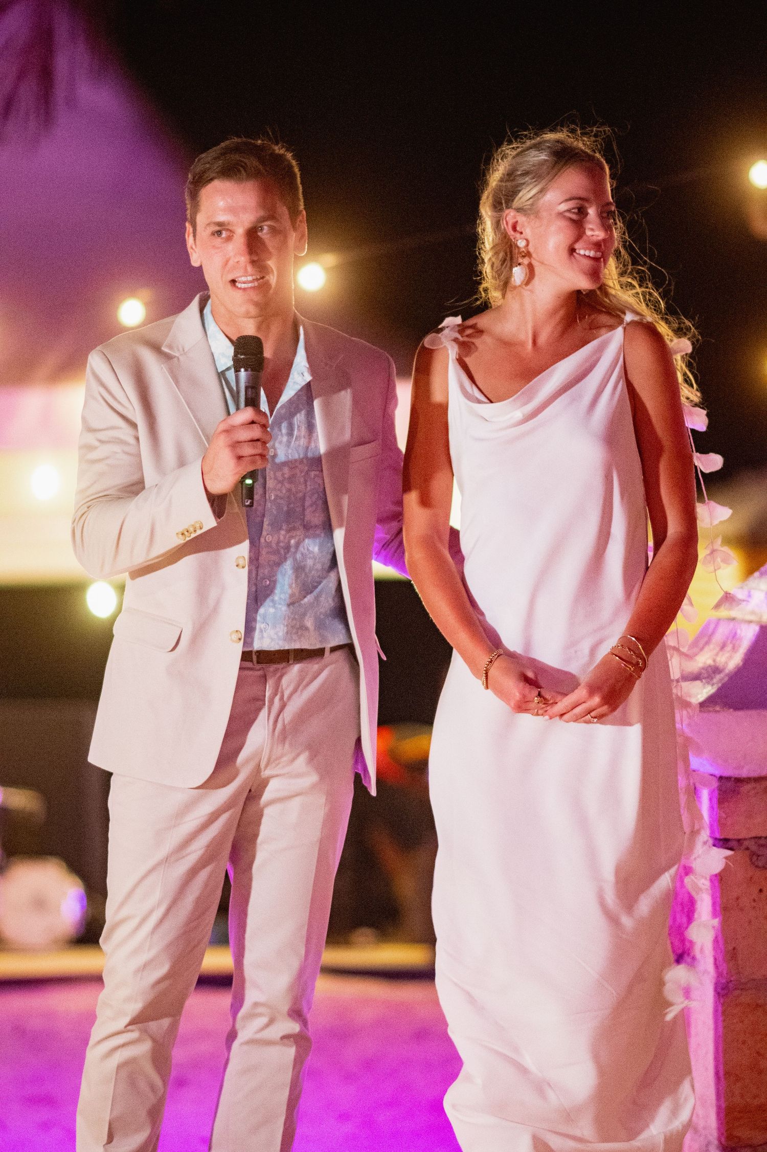 A couple dancing together at a wedding reception with purple lighting and white attire.