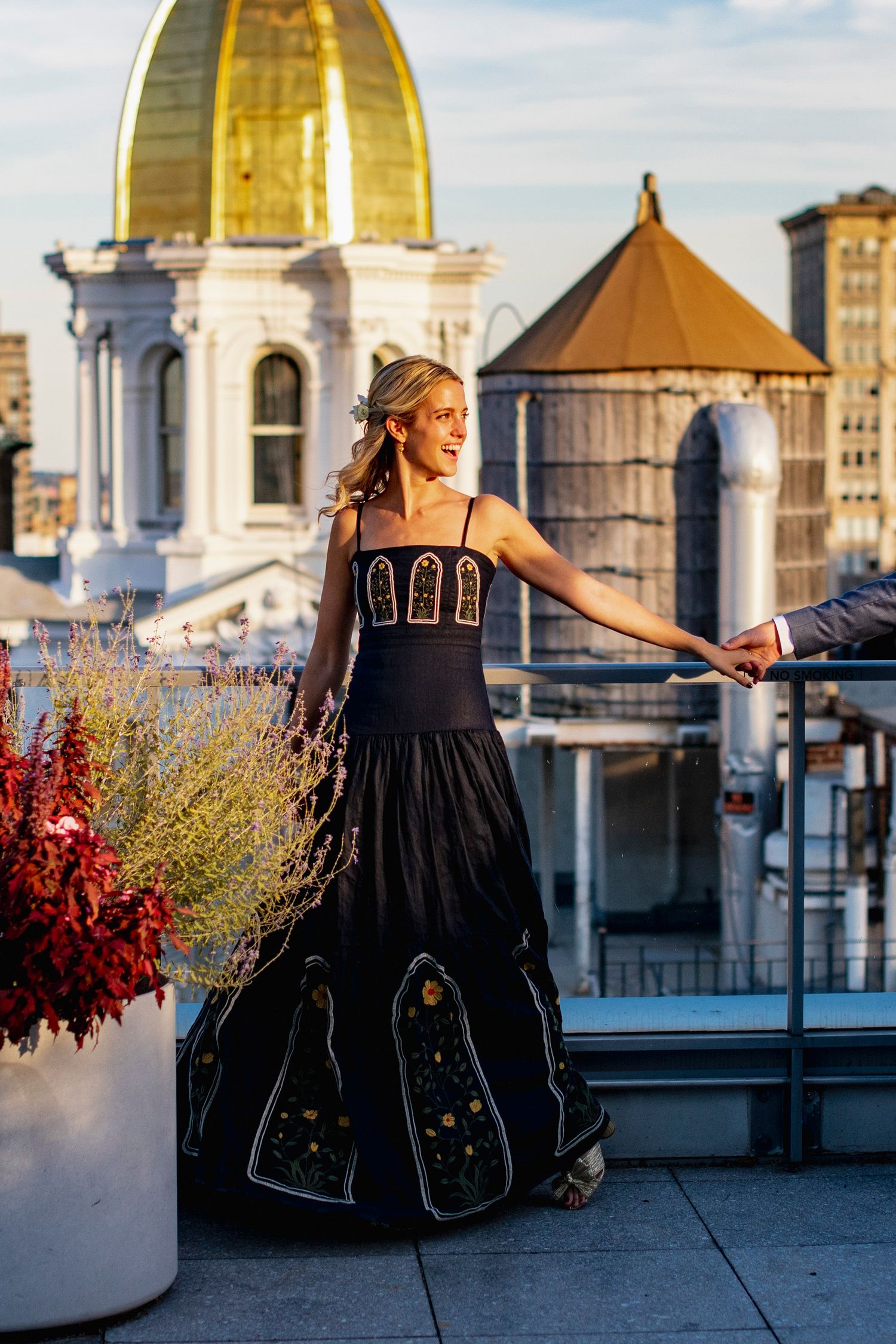 Woman in elegant black dress poses against city skyline with golden dome.
