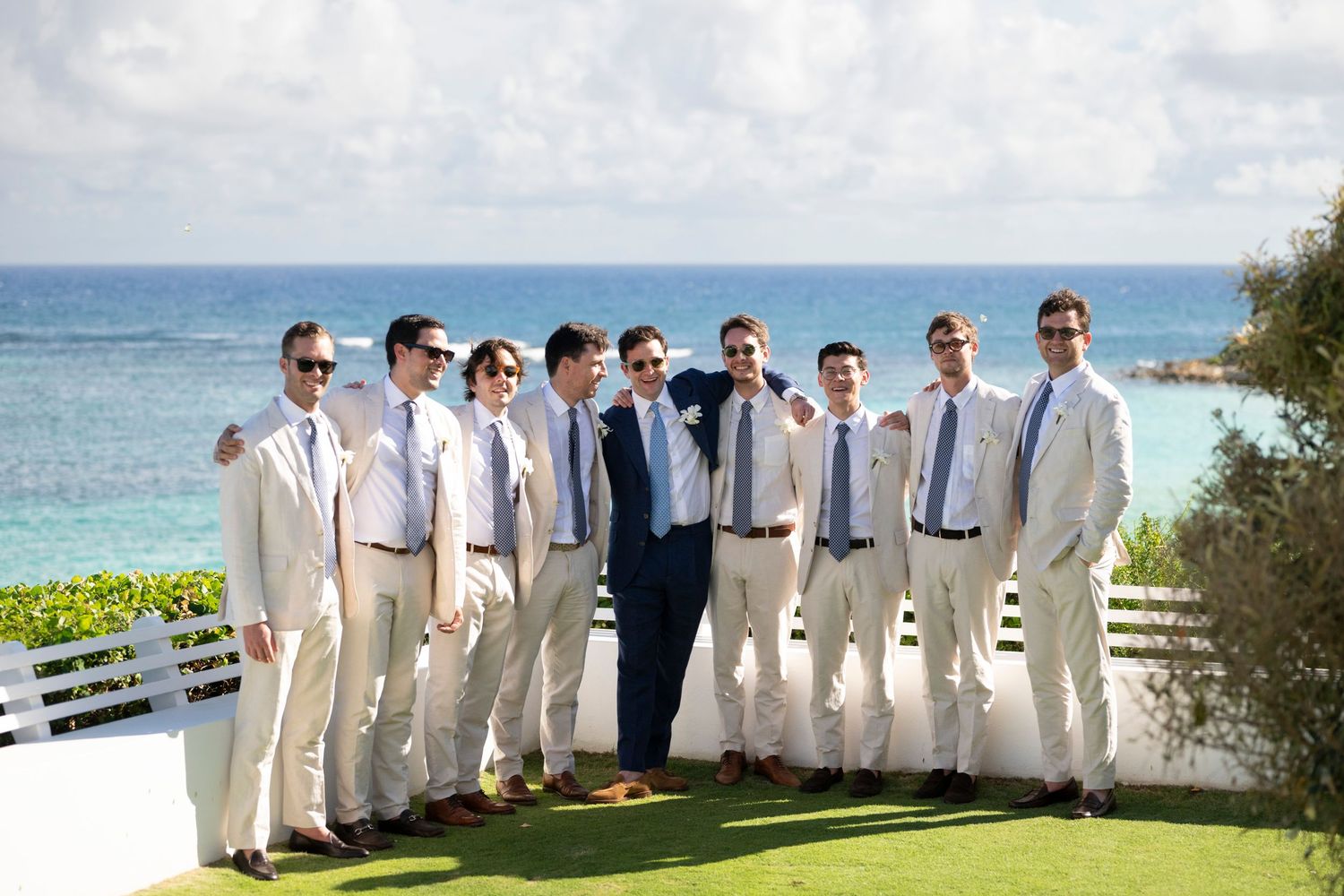 Groomsmen in light colored suits lined up against an ocean backdrop.