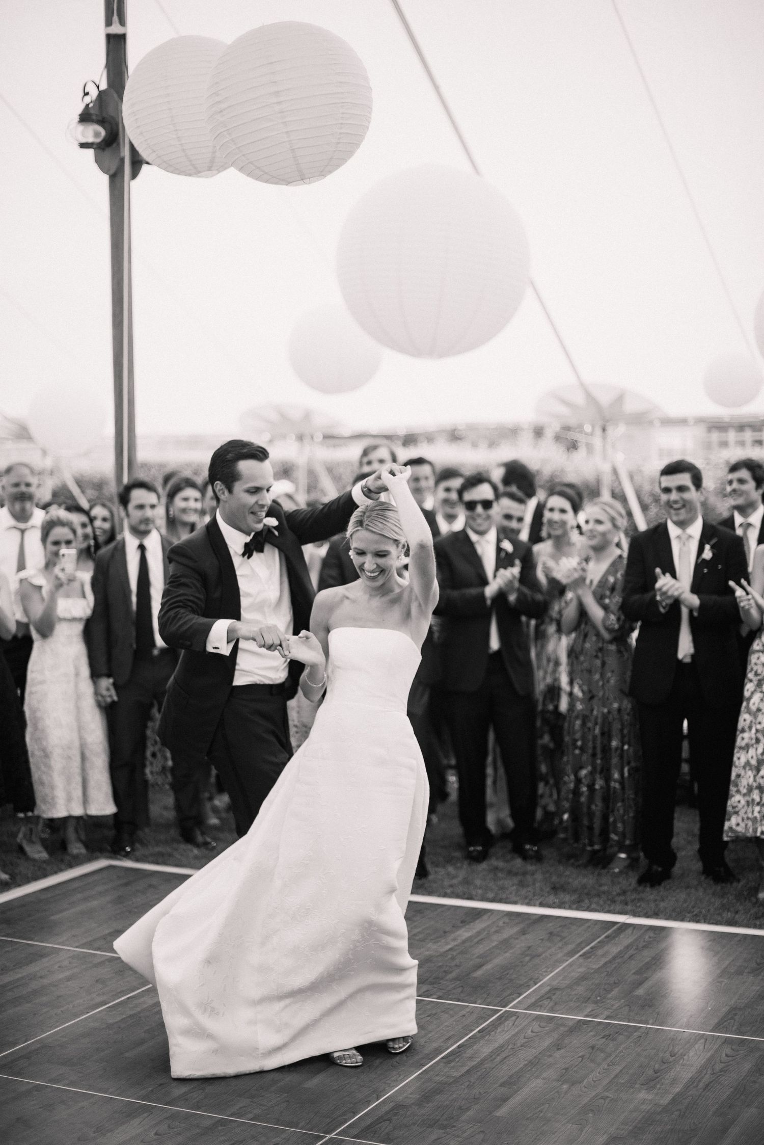 Black and white photo of wedding celebration dancing under a tent with paper lanterns.