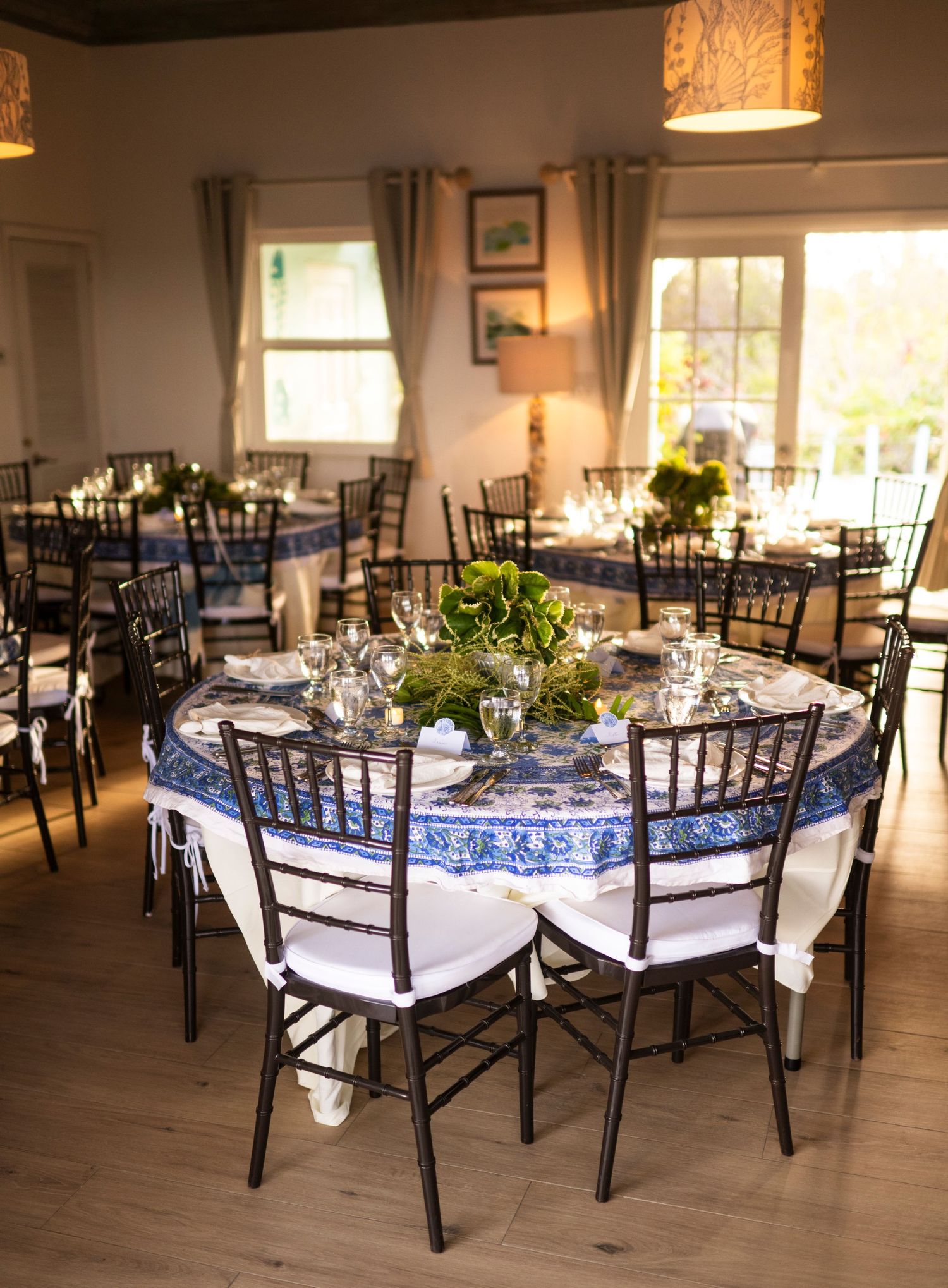Elegant wedding reception venue with blue and white table settings and dark wooden chairs in a bright indoor space.