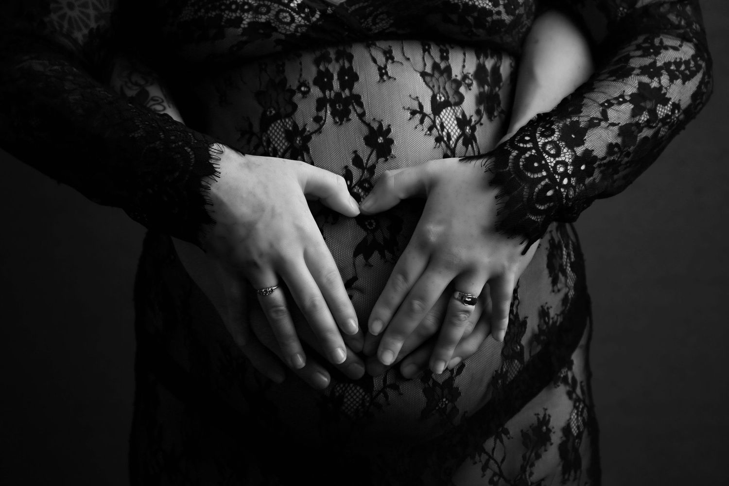 A beautiful maternity image of parents' hands forming a heart shape over the bump, full of love and anticipation.