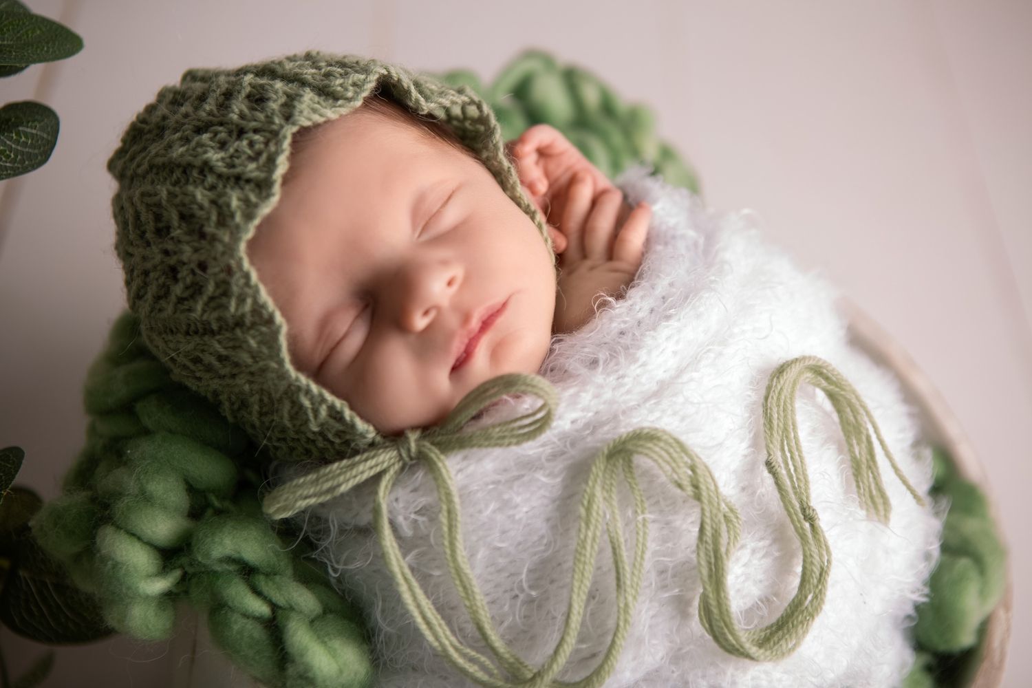 Newborn baby boy wrapped in soft white fluffy wrap with a green woven hat delicate and beautifully placed over the wrap.