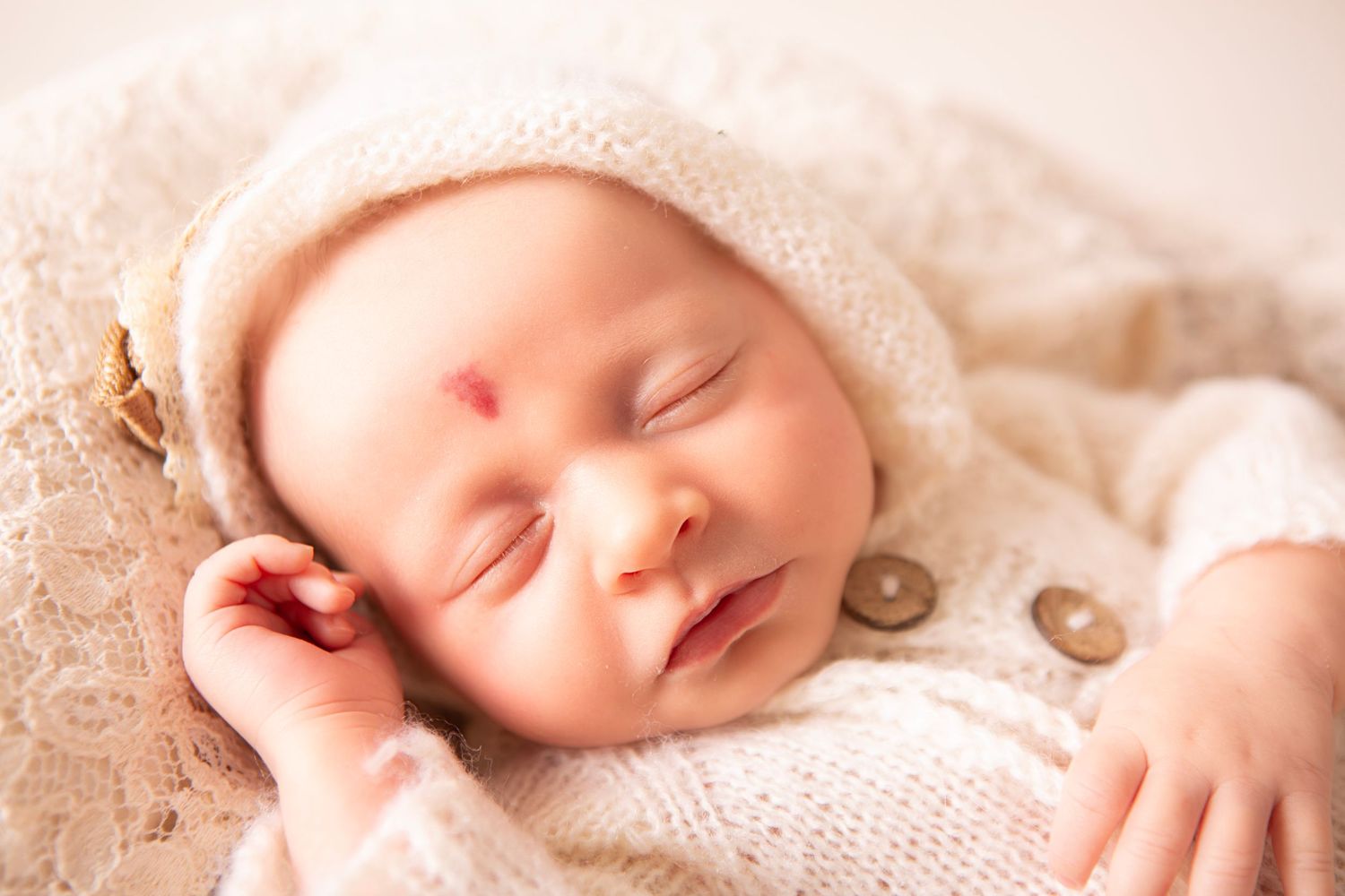 Peaceful sleeping newborn baby wearing a cream knit hat, wrapped in soft white blanket.