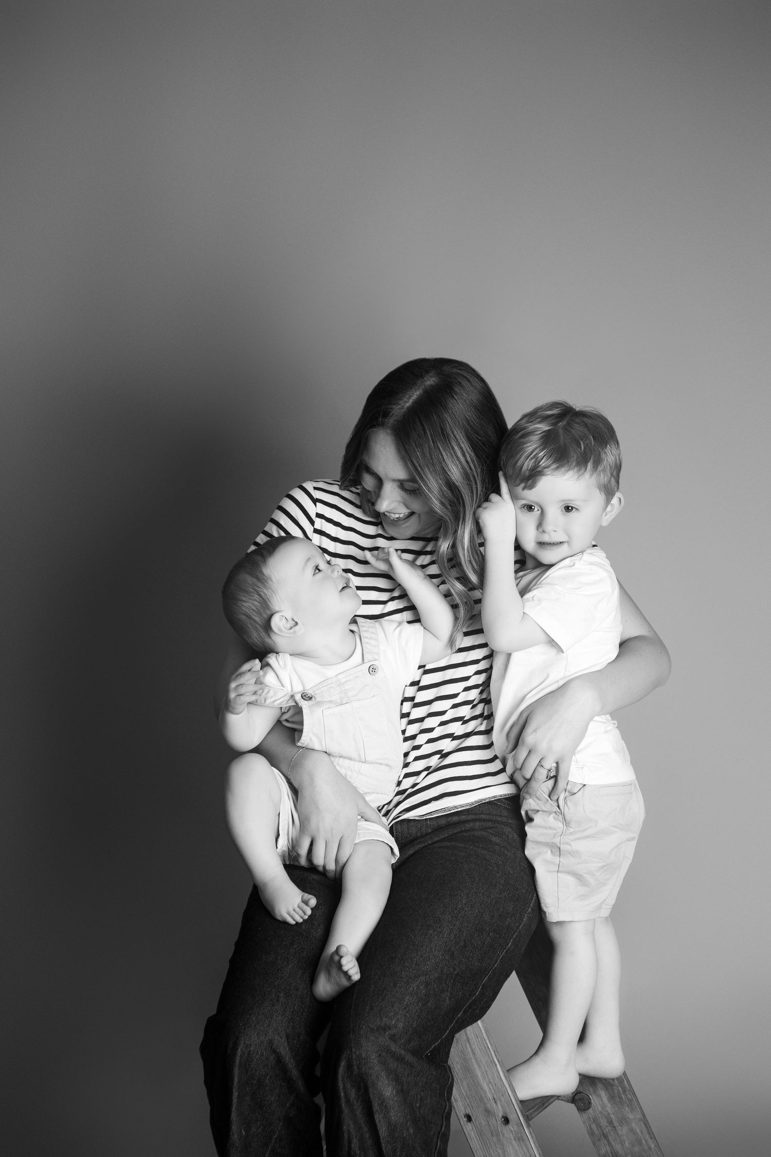Black and white photo of a smiling mother sitting with her two young sons, sharing a tender family moment.
