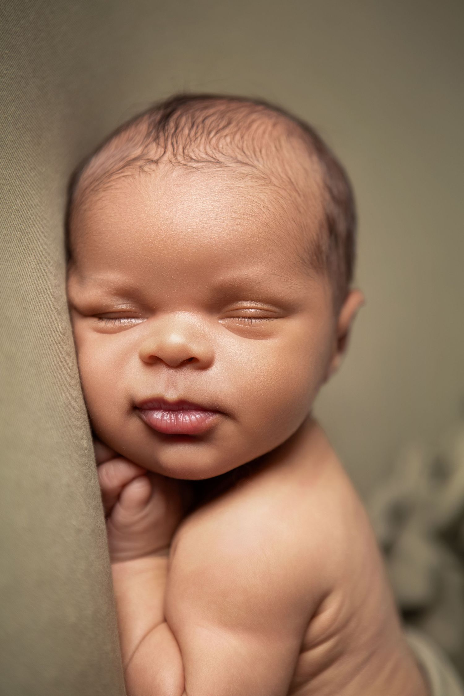 A simple, striking newborn portrait of baby boy's face against a soft khaki green backdrop.