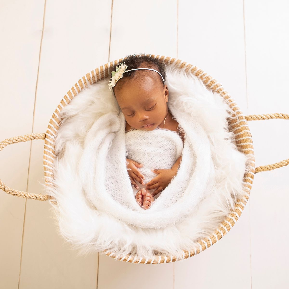 Sleeping newborn baby wrapped in white lace in a round wicker basket with fluffy white fur lining.