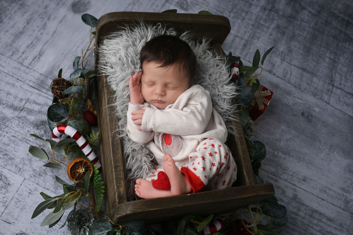 Newborn baby sleeping in a rustic wooden crib with Christmas decorations and candy canes.