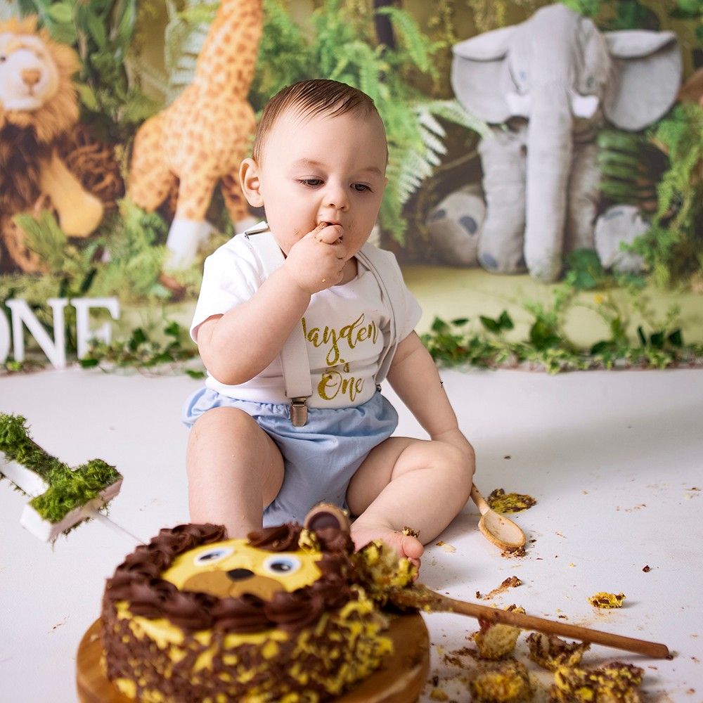 Baby boy enjoys his first birthday cake smash with a lion cake and jungle safari themed backdrop.