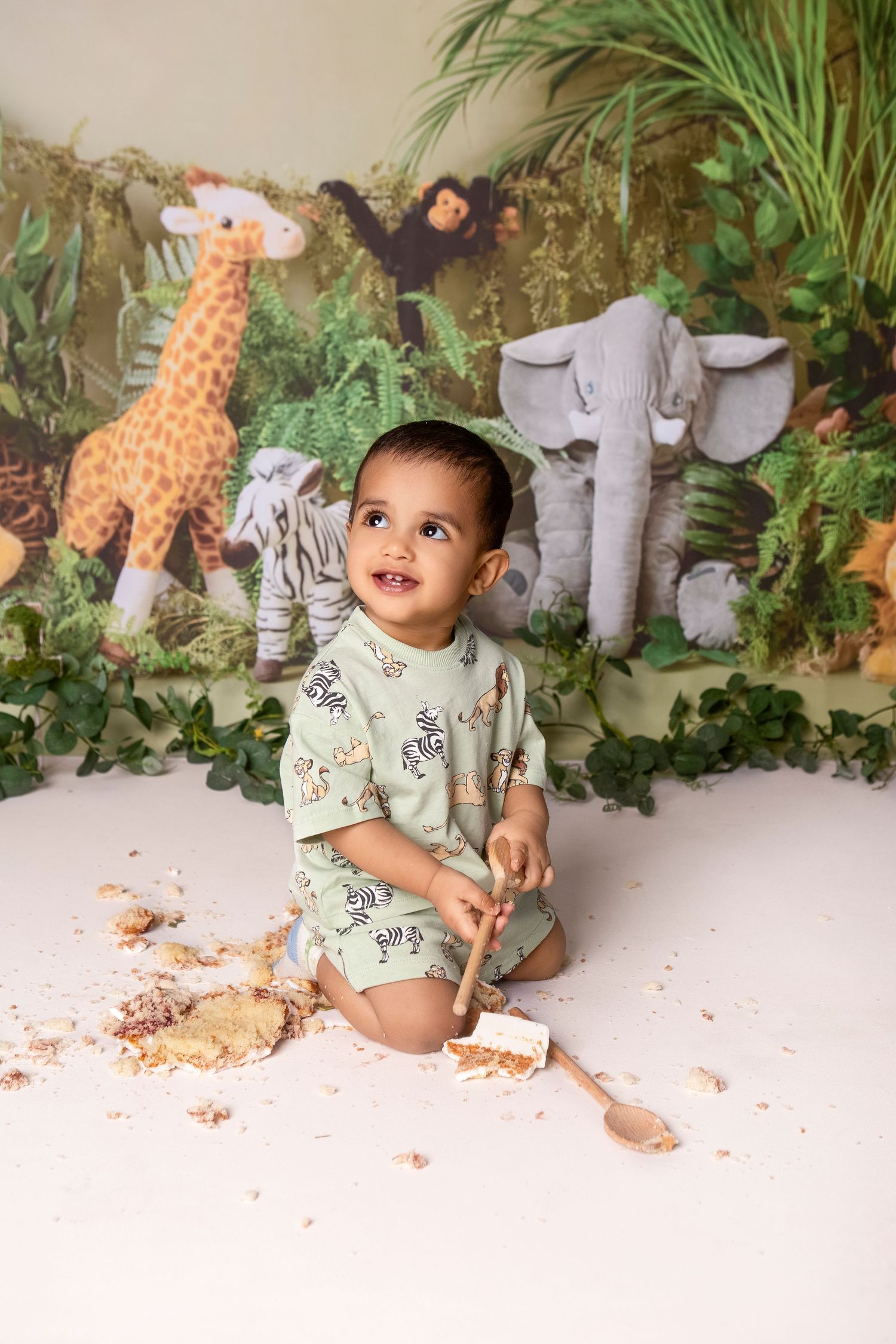 Baby boy in safari romper smiling during jungle themed cake smash birthday photo session.