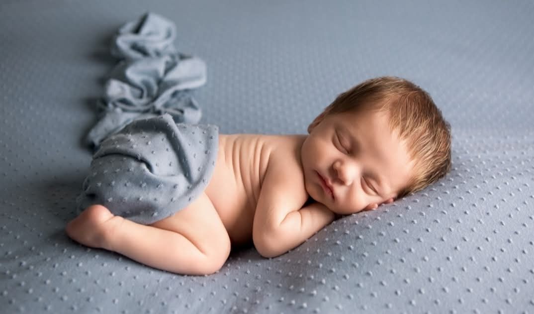 A sweet newborn portrait of baby boy posed on a soft blue spotted backdrop, simple and timeless.