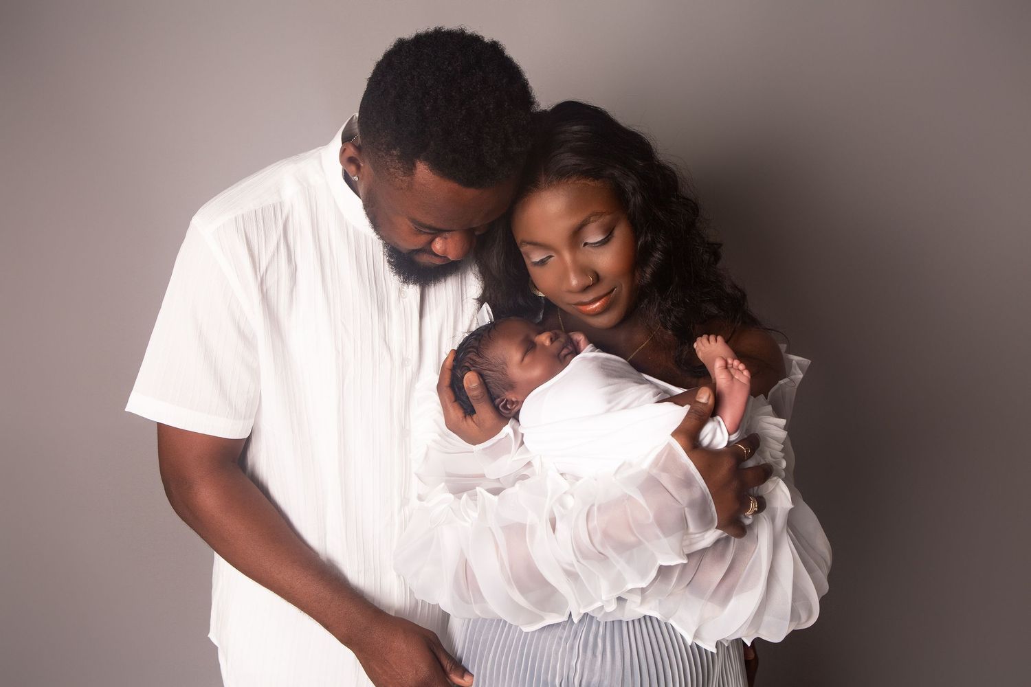 A tender newborn portrait of mum and dad holding their baby close, full of love and quiet connection.