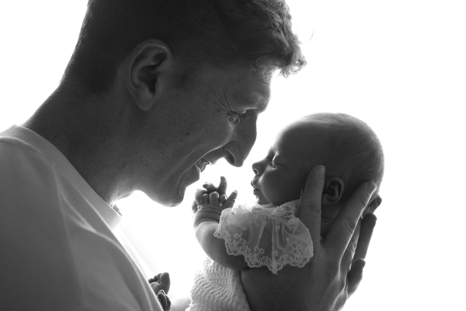 Black and white photo of a smiling man tenderly holding a newborn baby close to his face.