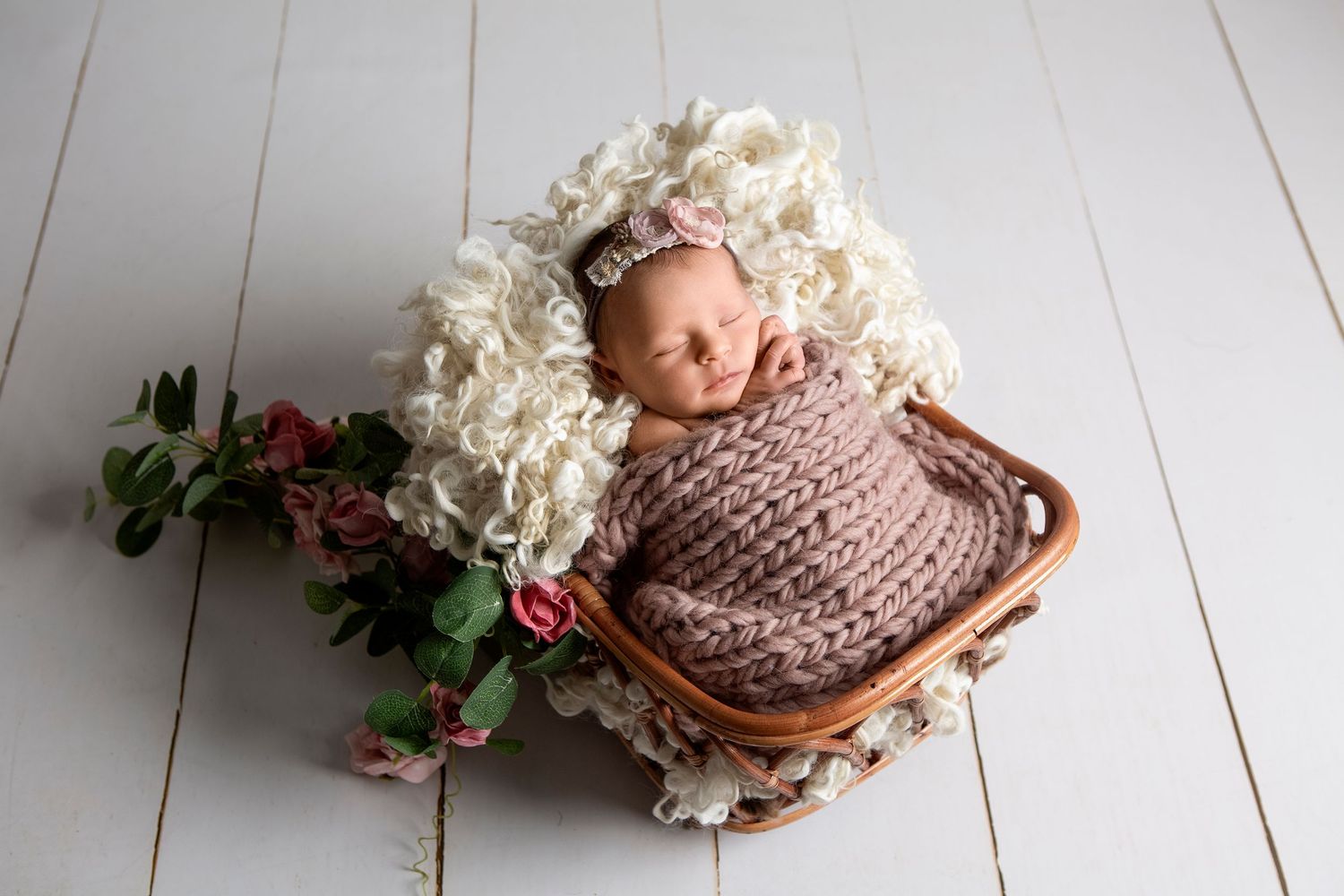 A delicate newborn portrait of baby girl in a basket with a dusty rose blanket, fingers gently resting by her face.