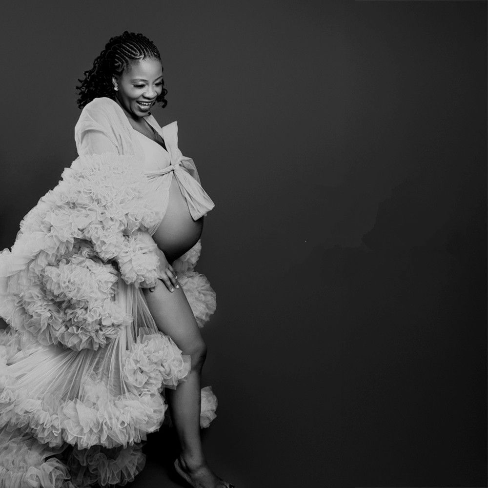 Black and white maternity photo of a smiling pregnant woman in a fluffy robe, elegantly posing in a studio setting.