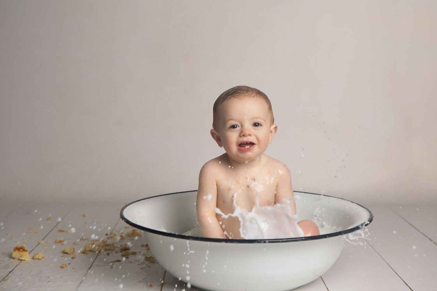 Happy baby splashing in a white enamel wash basin during a professional photo session.