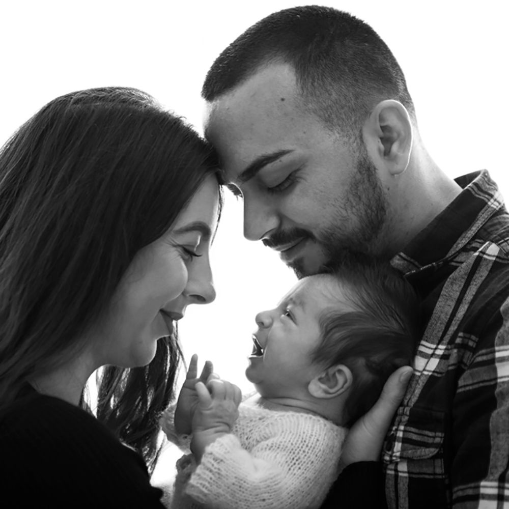 Black and white photo of smiling parents lovingly holding their laughing newborn baby close together.