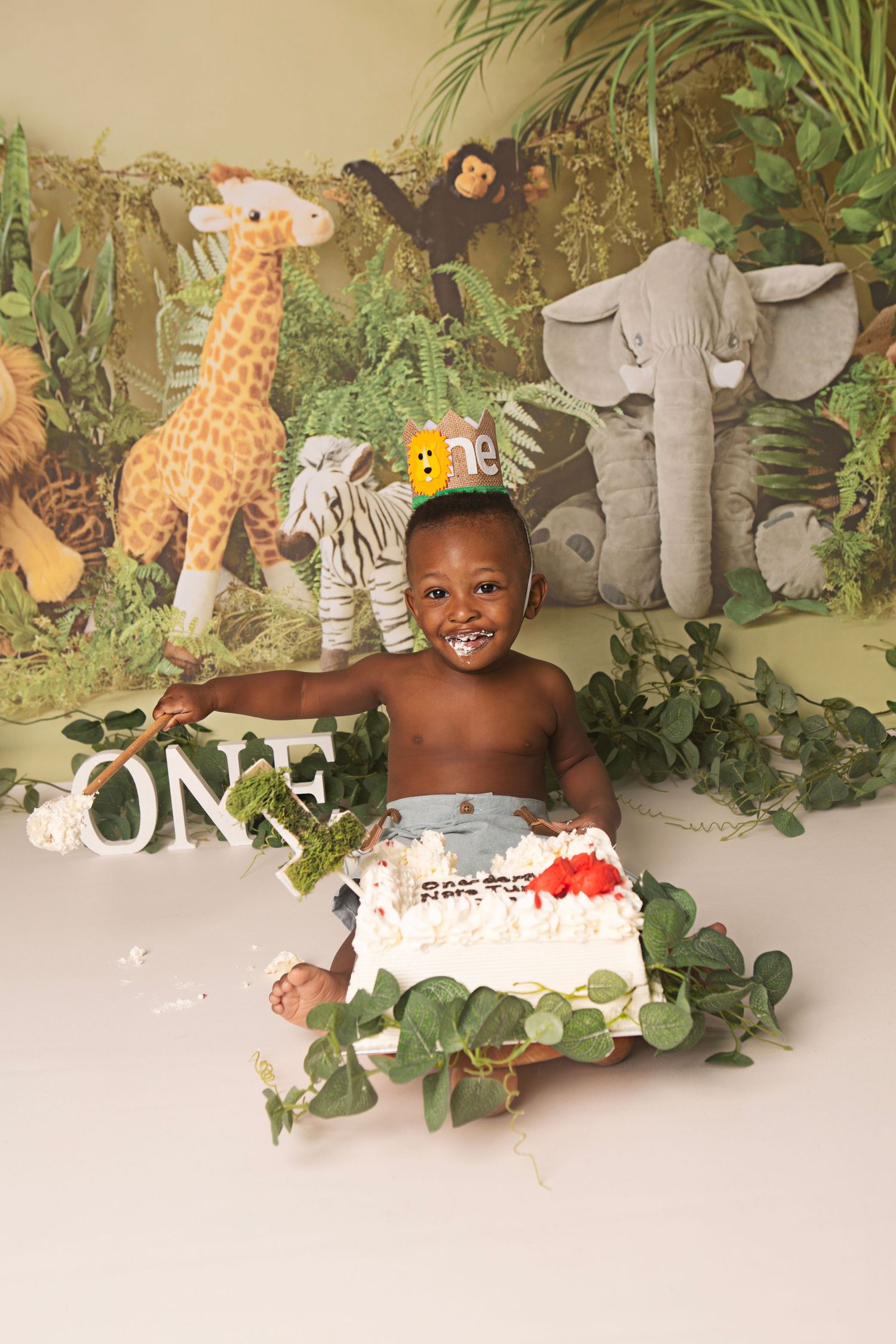 Baby's first birthday cake smash with jungle safari backdrop featuring giraffe, elephant, and zebra decorations.