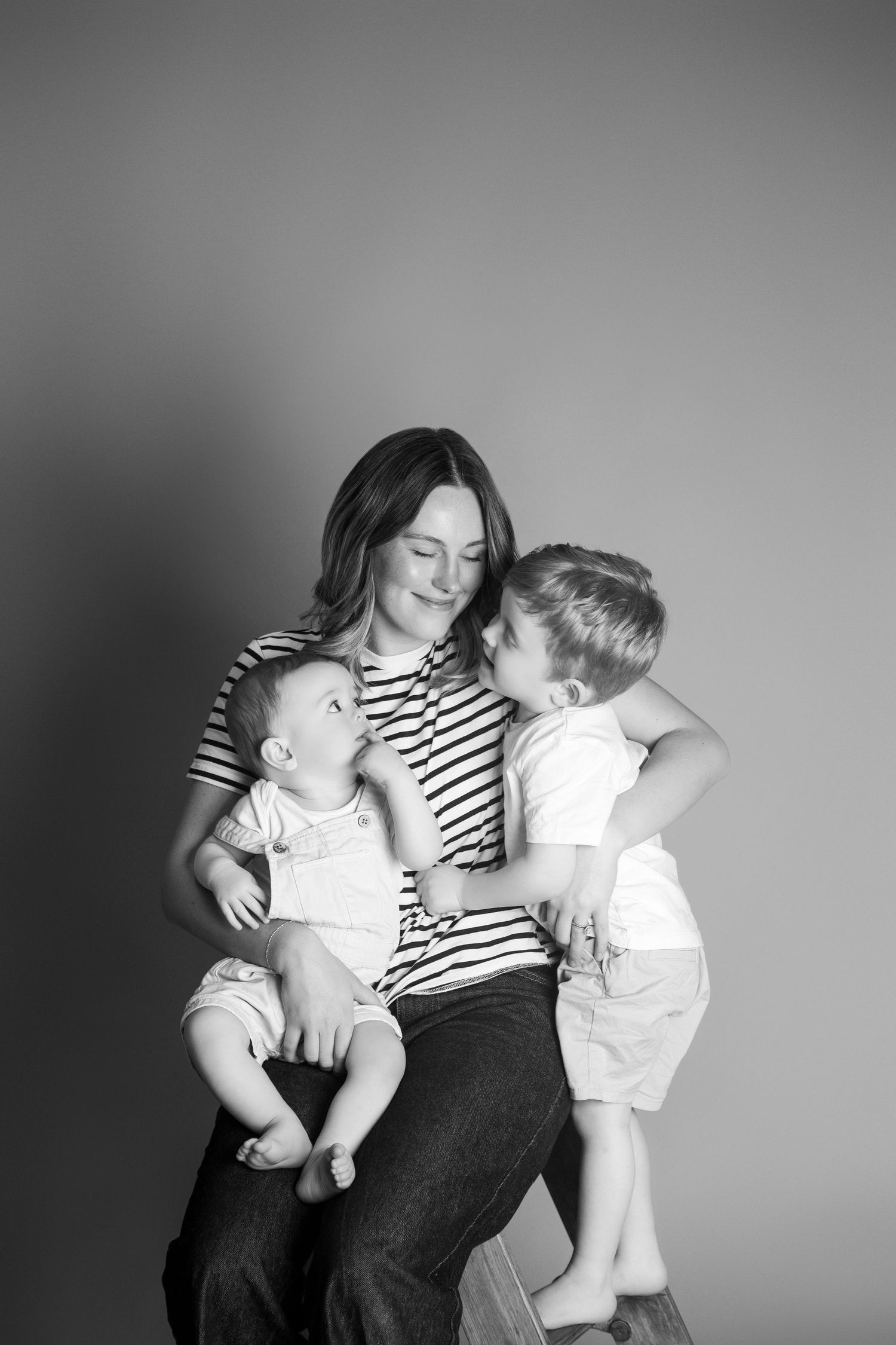 Black and white photo of a mother sitting with her baby and young son in a warm family portrait studio session.