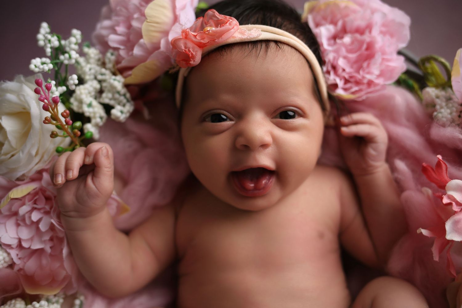 A joyful image of baby girl laughing, surrounded by soft pink flowers, full of happiness and charm.