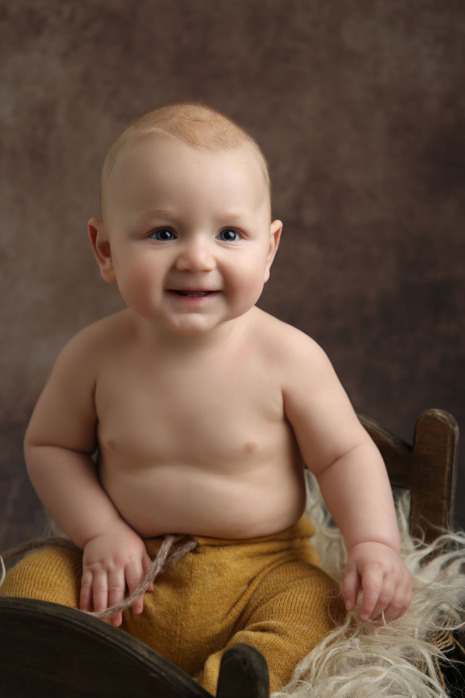Smiling baby sitting in a wooden crate with mustard yellow knit pants and fluffy fur lining.