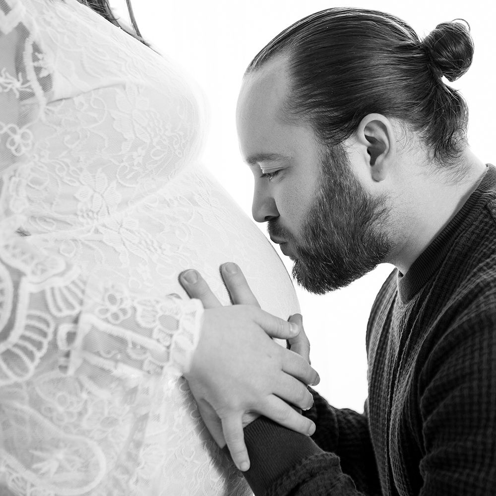 Black and white photo of a bearded man with a bun hairstyle carefully examining intricate white lace fabric.