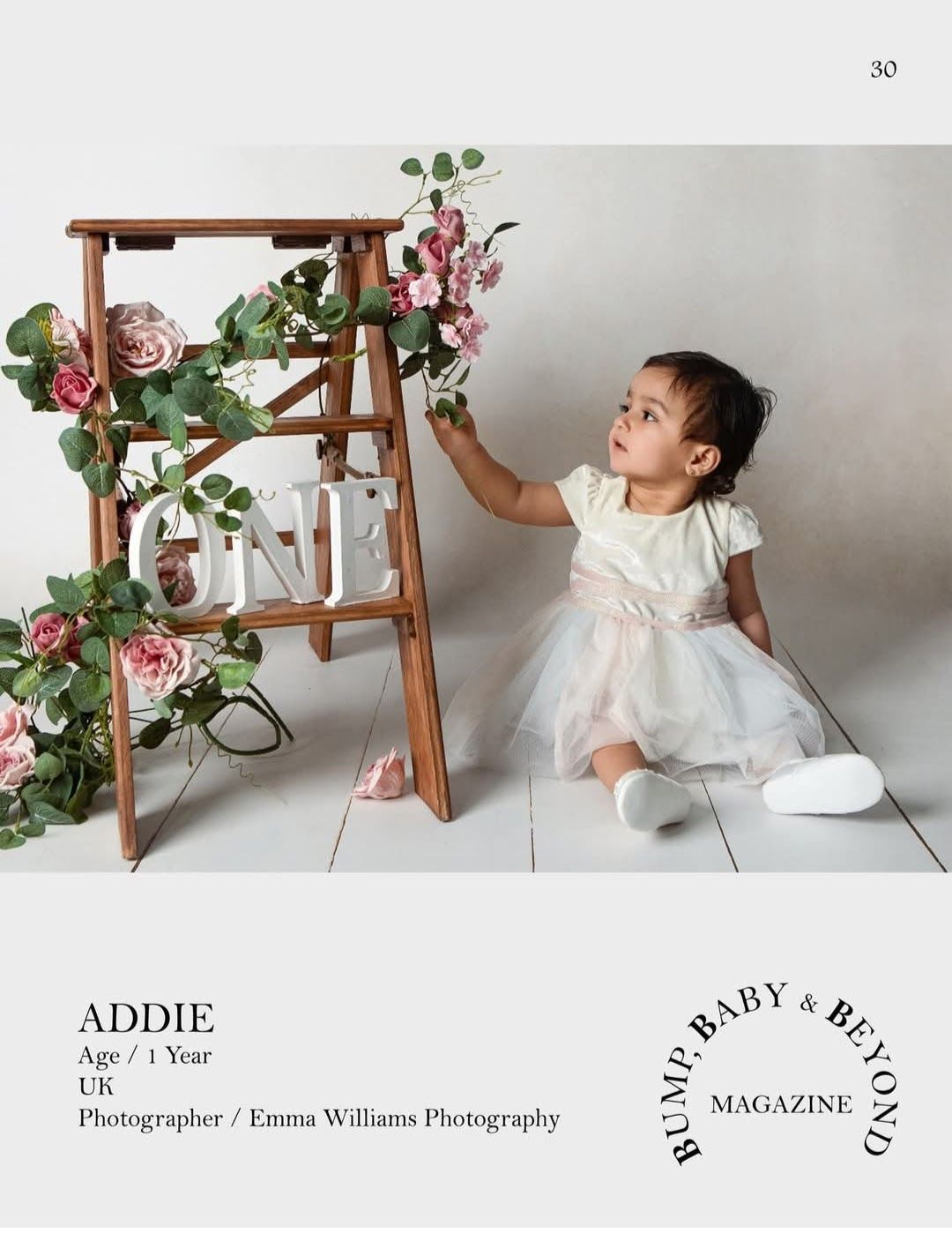 One-year-old Addie in a white dress reaching for flowers on a decorated ladder in a UK photography shoot.