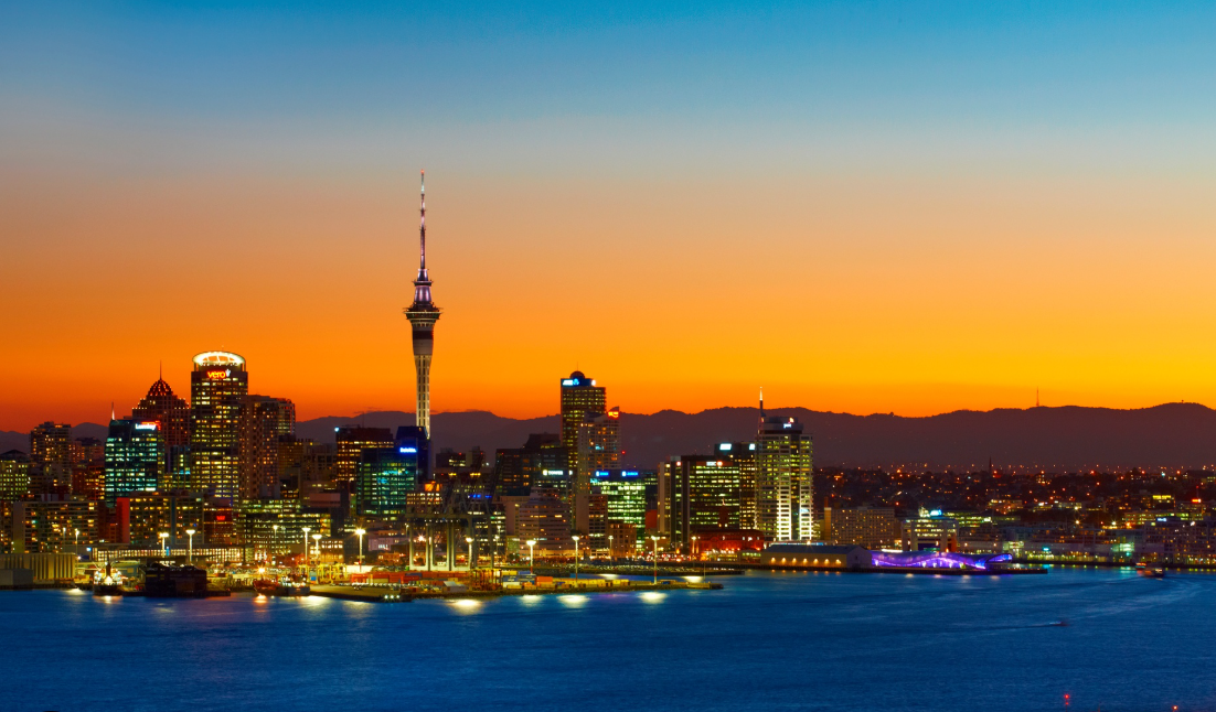 Auckland city skyline illuminated at sunset with the Sky Tower reflected over the harbor waters.