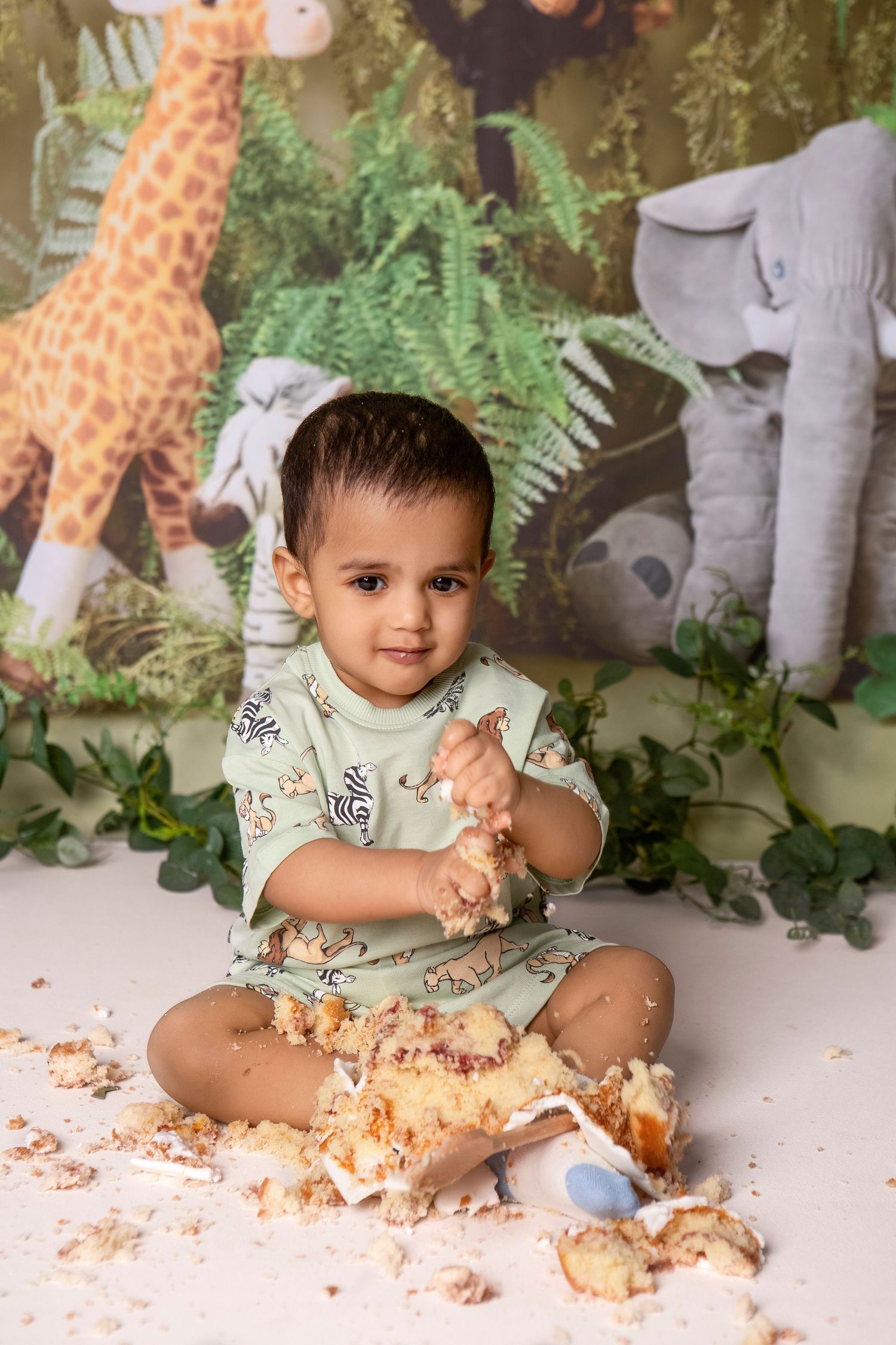Toddler boy eating smash cake at jungle safari themed first birthday photography session.