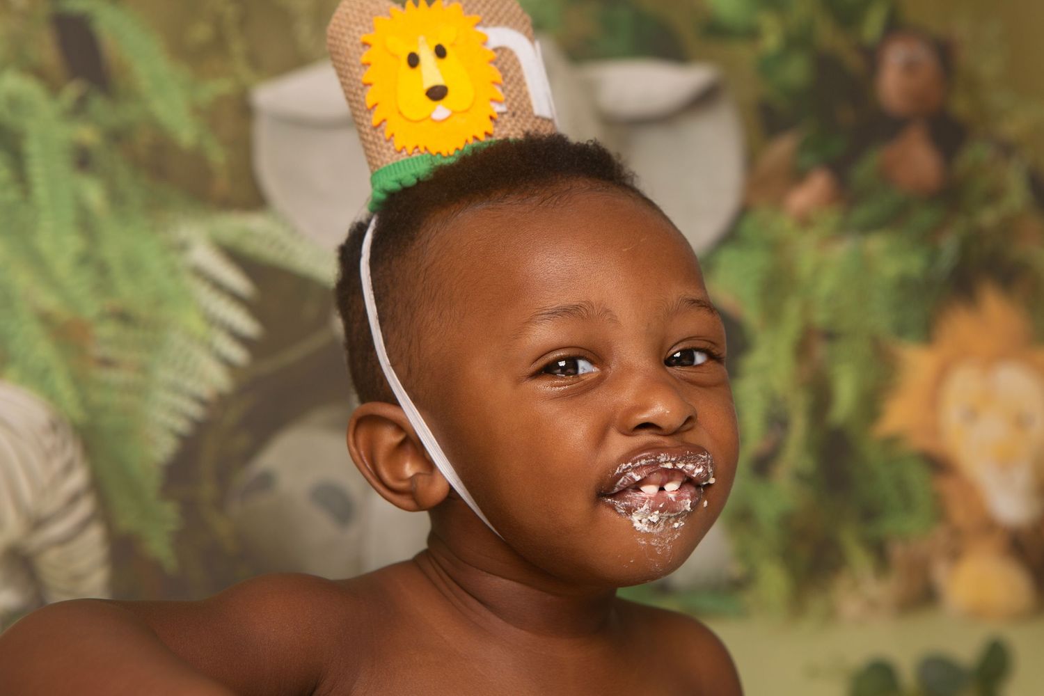Joyful young child wearing a sunflower headband with frosting on face, celebrating a birthday party.