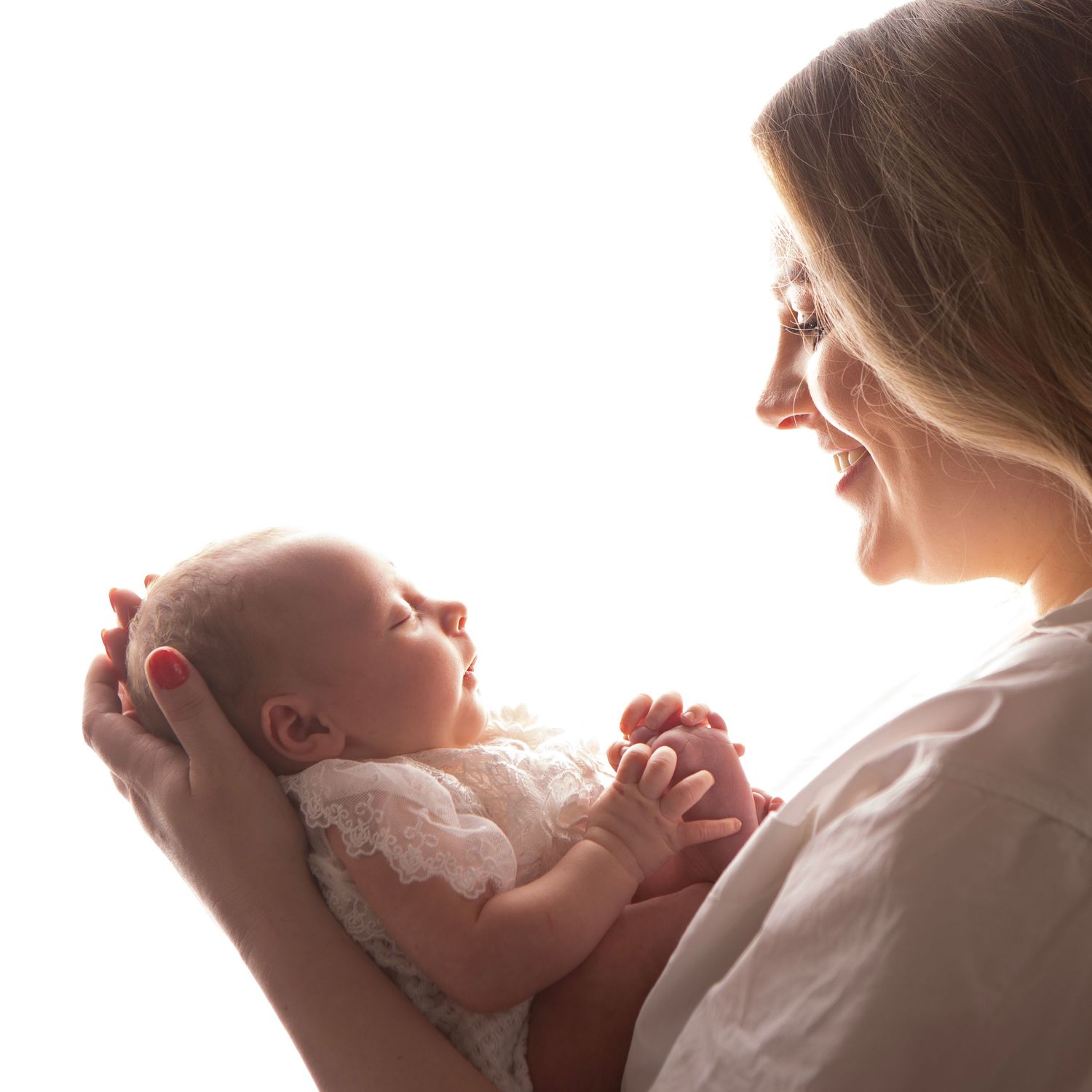 A smiling mother gently holds her newborn baby in her arms against a bright white background.