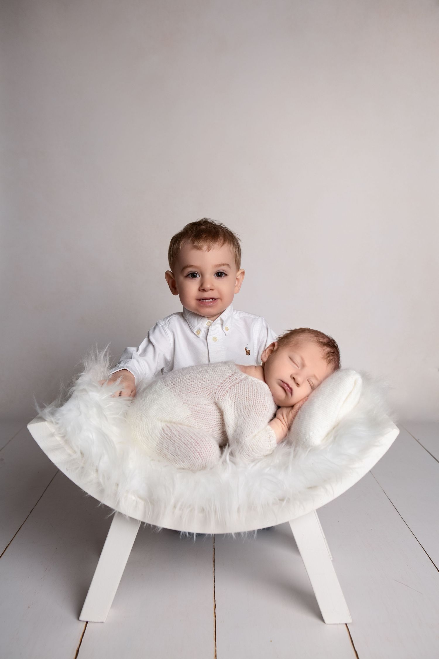 A tender newborn portrait featuring big brother watching over his sleeping baby sibling in front.