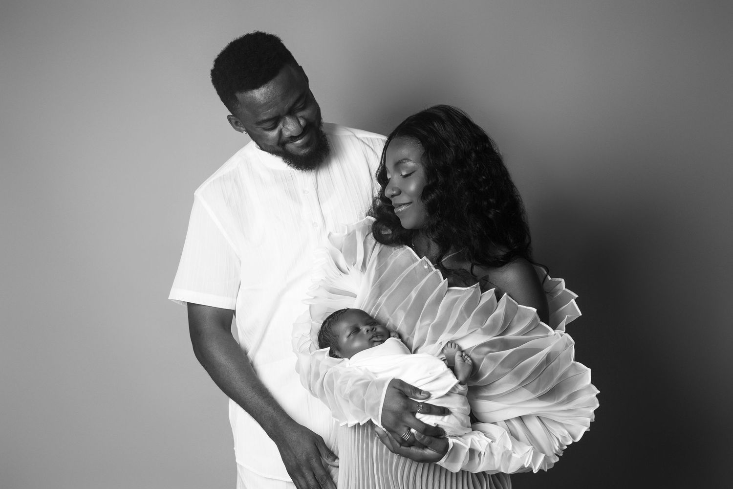 Black and white portrait of proud parents tenderly holding their newborn baby in studio photography.