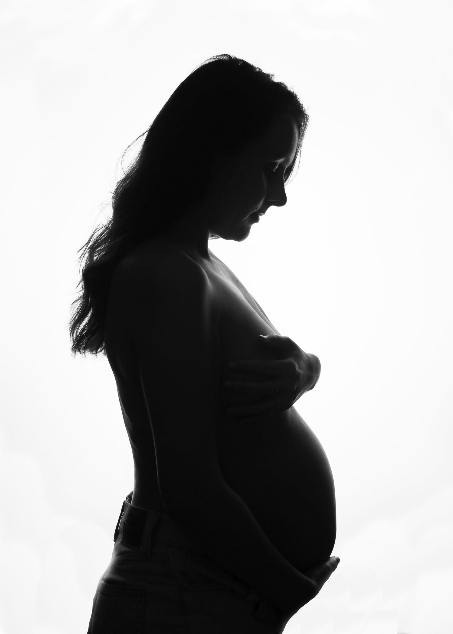 Black and white silhouette of a pregnant woman cradling her baby bump against a white background.