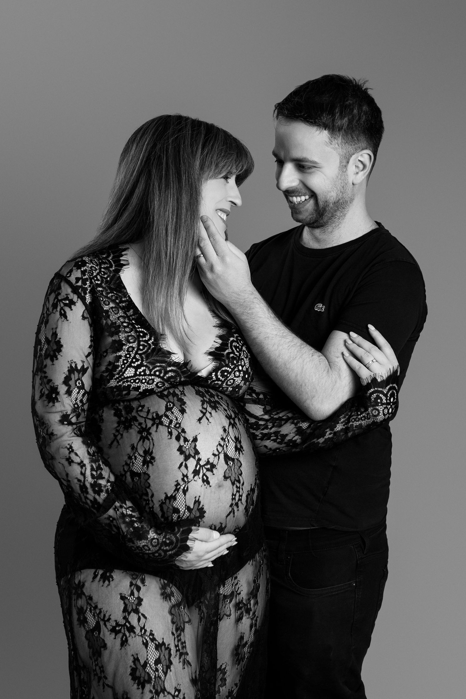 Black and white photo of man tenderly touching pregnant partner's face as she cradles her belly.