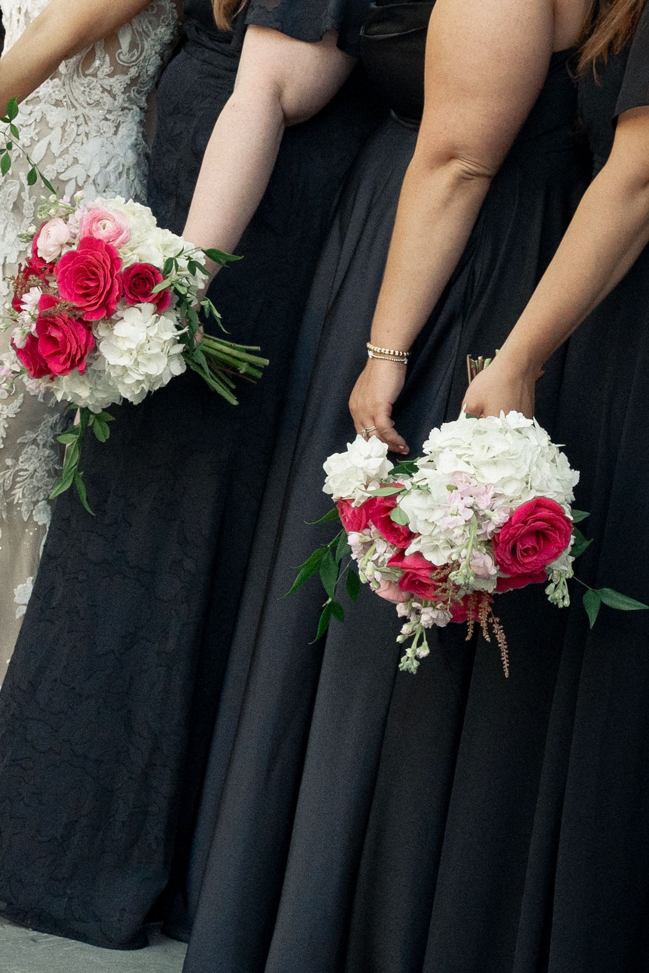 Close-up of bridesmaids in navy gowns holding elegant bouquets of pink roses and white hydrangeas.