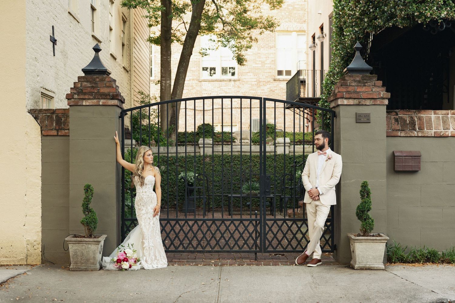 Bride and groom posing elegantly at ornate iron gates outside a historic building on their wedding day.