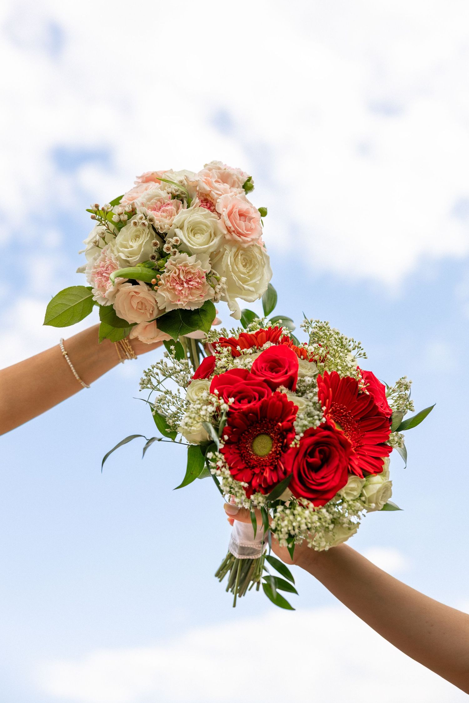Two hands holding pink and red rose bouquets raised against a blue sky.