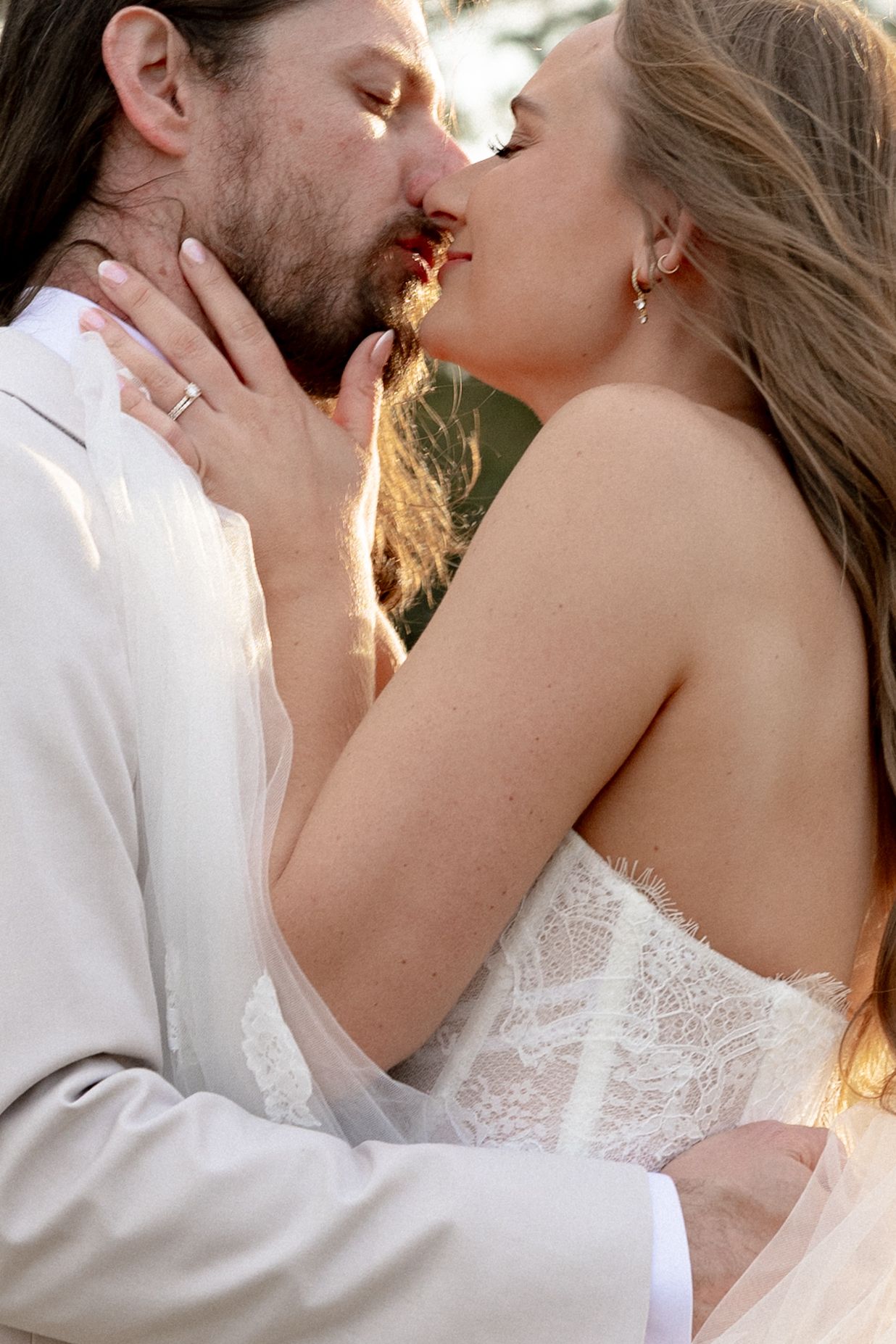 Close-up of bride and groom sharing a passionate kiss in warm golden sunset light.