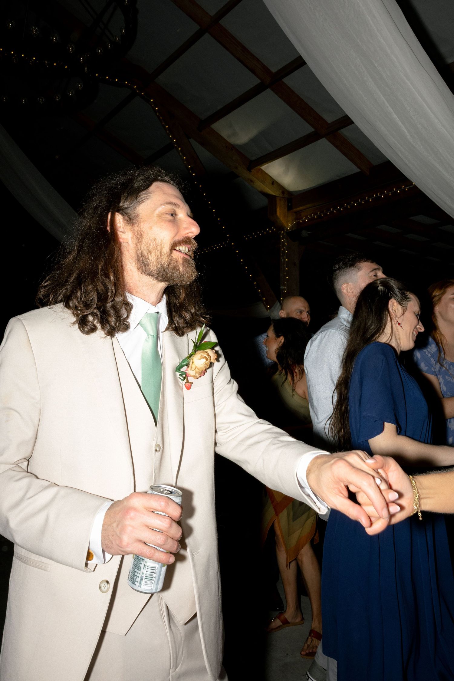 Groom in beige suit with mint tie and boutonniere smiling at wedding reception.
