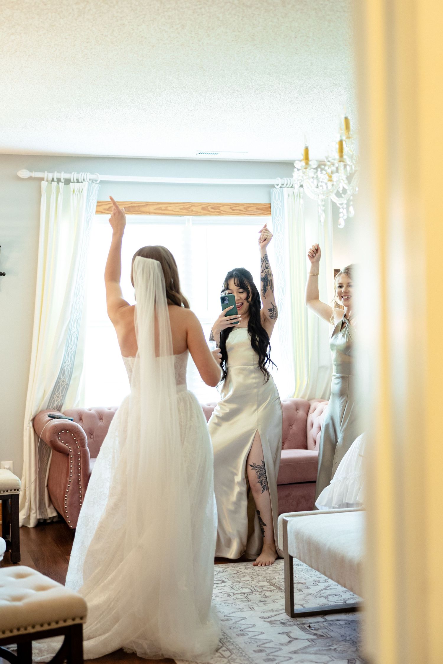Bride and bridesmaid celebrating with arms raised, reflected in mirror during wedding preparations.