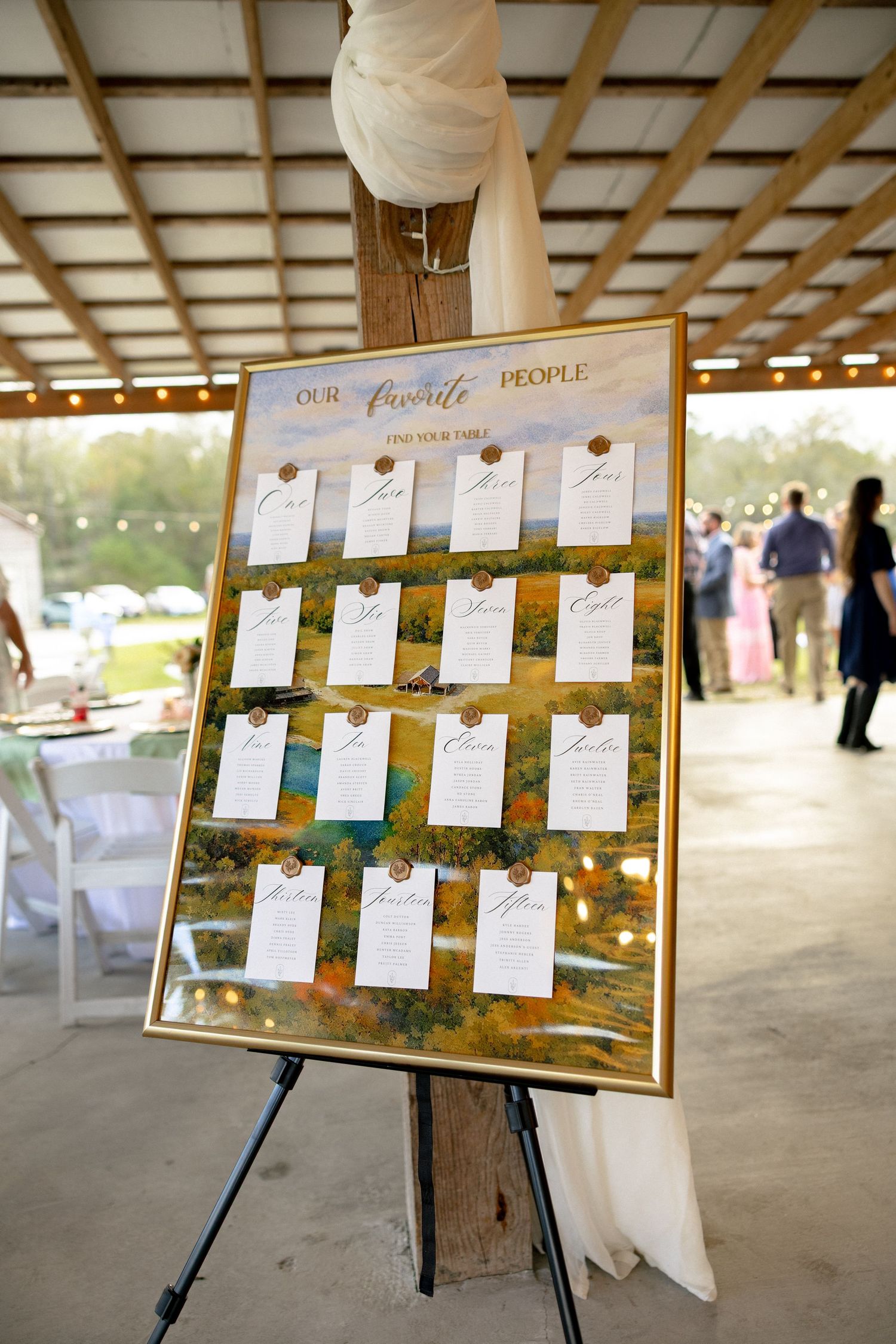 Gold-framed wedding seating chart labeled Our Favorite People displayed on an easel inside a barn venue.