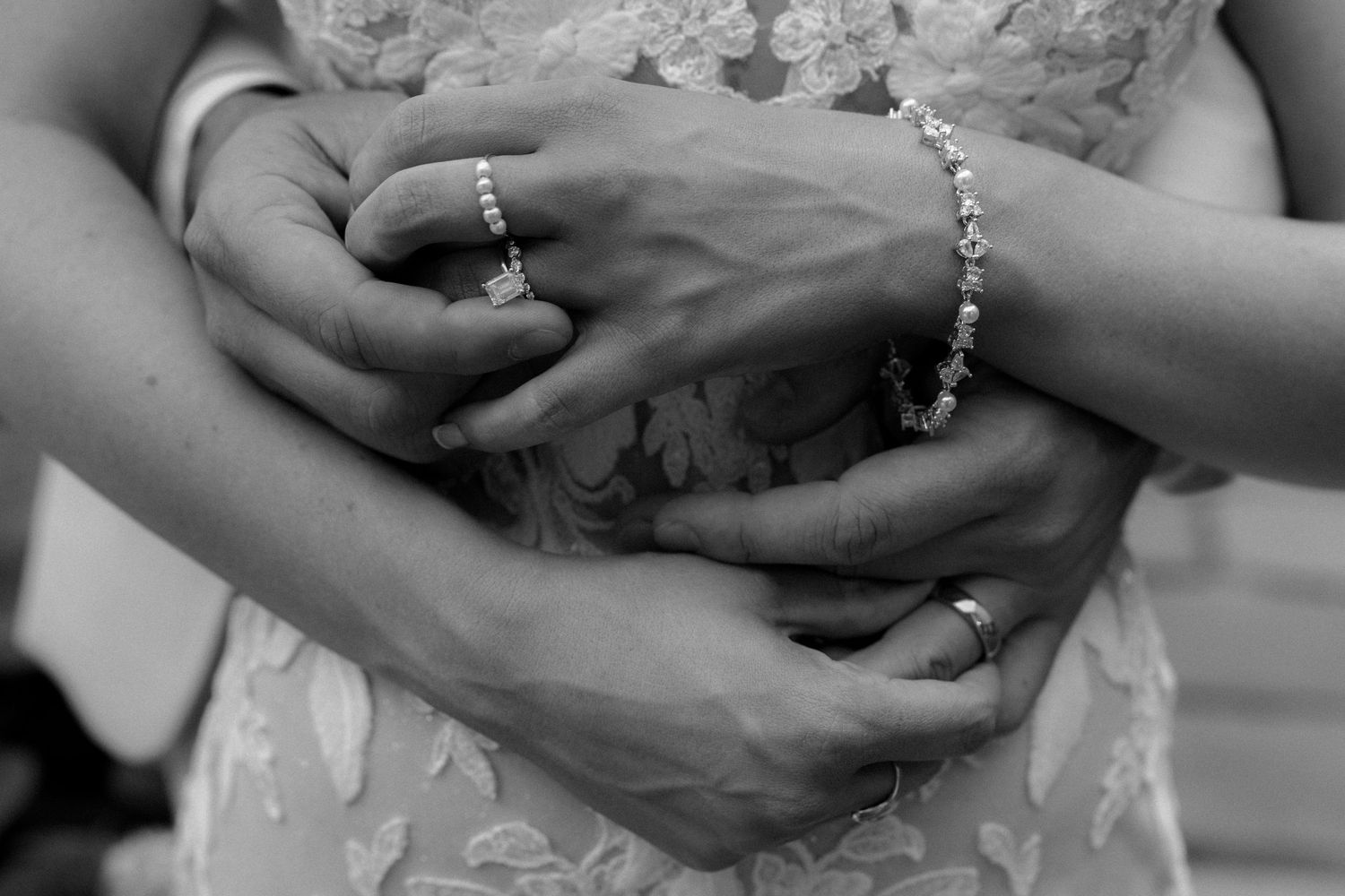 Black and white close-up of newlyweds hands clasped together wearing wedding rings and diamond bracelet.