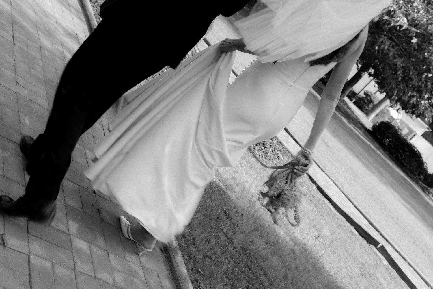 Black and white photo of a person in a flowing white dress standing outdoors on a paved surface.