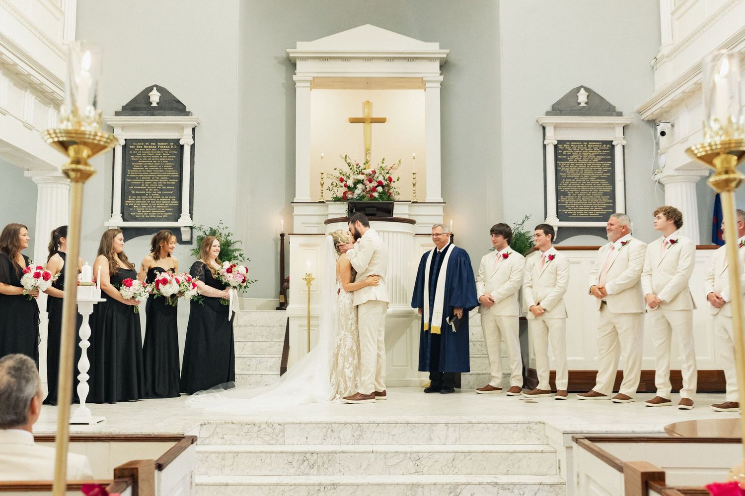 Wedding party stands at church altar as bride and groom exchange vows before officiant.
