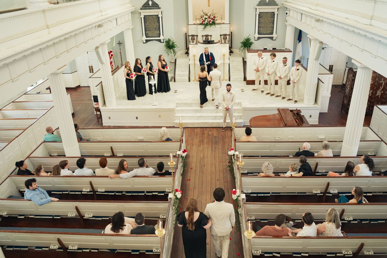 Aerial view of a traditional church wedding ceremony with guests seated in wooden pews and bridal party at the altar.