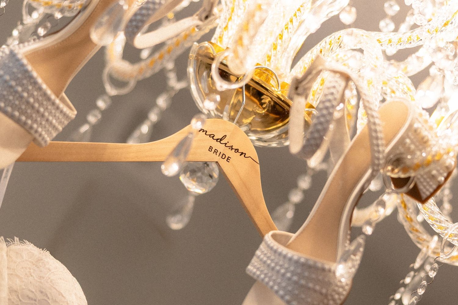 Pearl-embellished bridal heels hanging on personalized Madison Bride hanger from crystal chandelier.