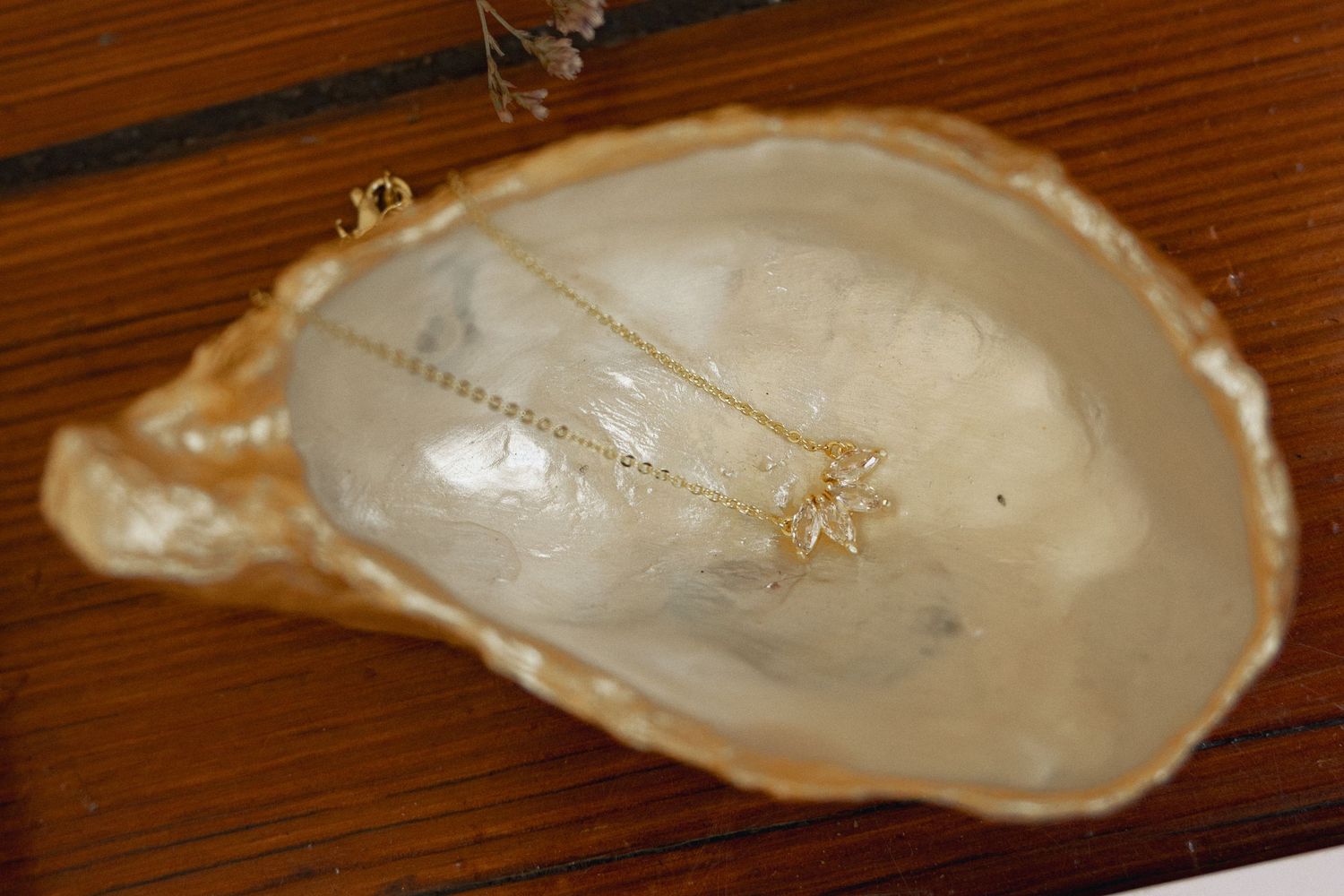 Delicate gold star pendant necklace displayed in a natural pearl oyster shell on wooden surface.