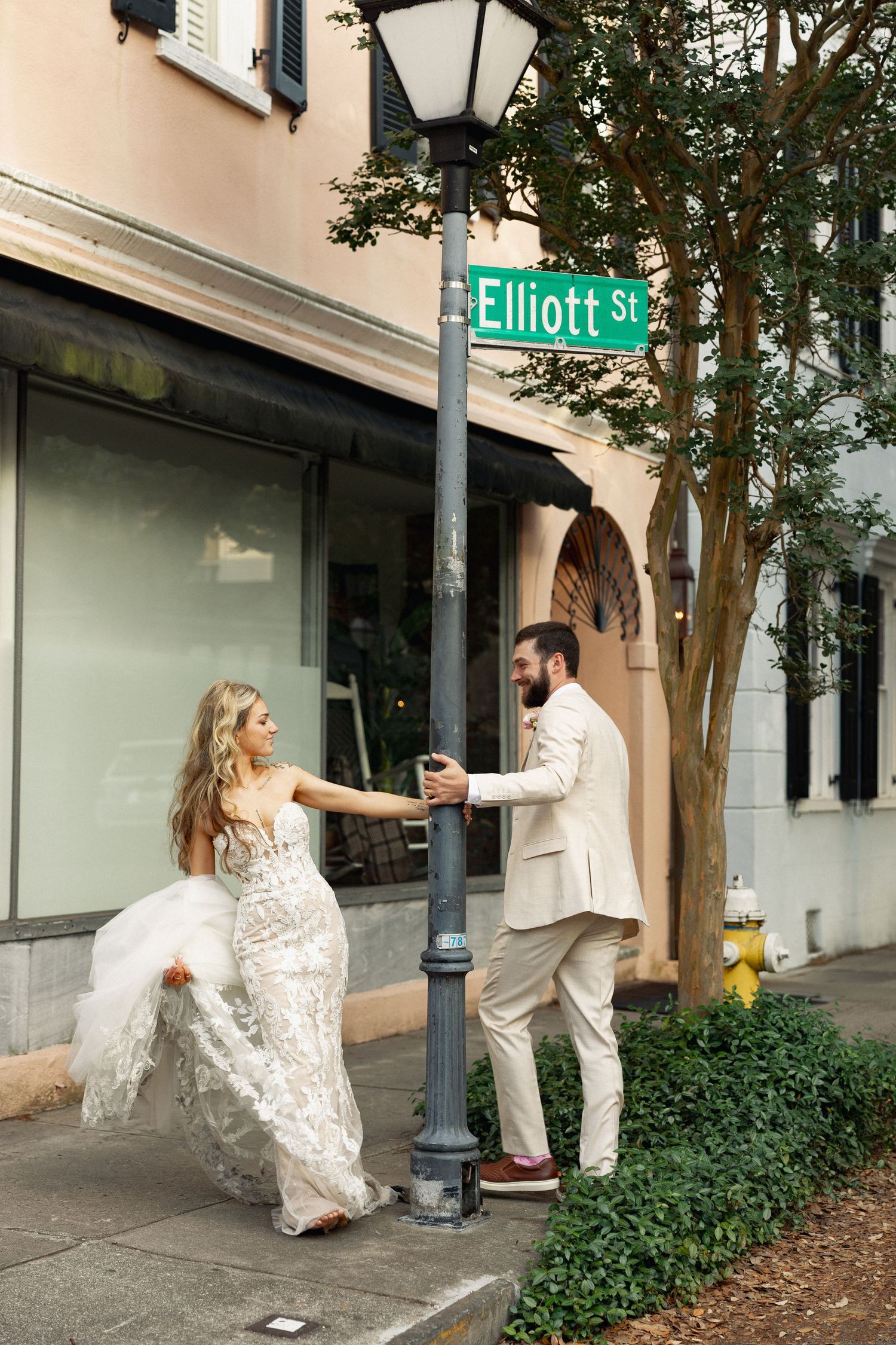 Bride and groom hold lamppost beneath Elliott St sign in charming downtown Charleston street corner.