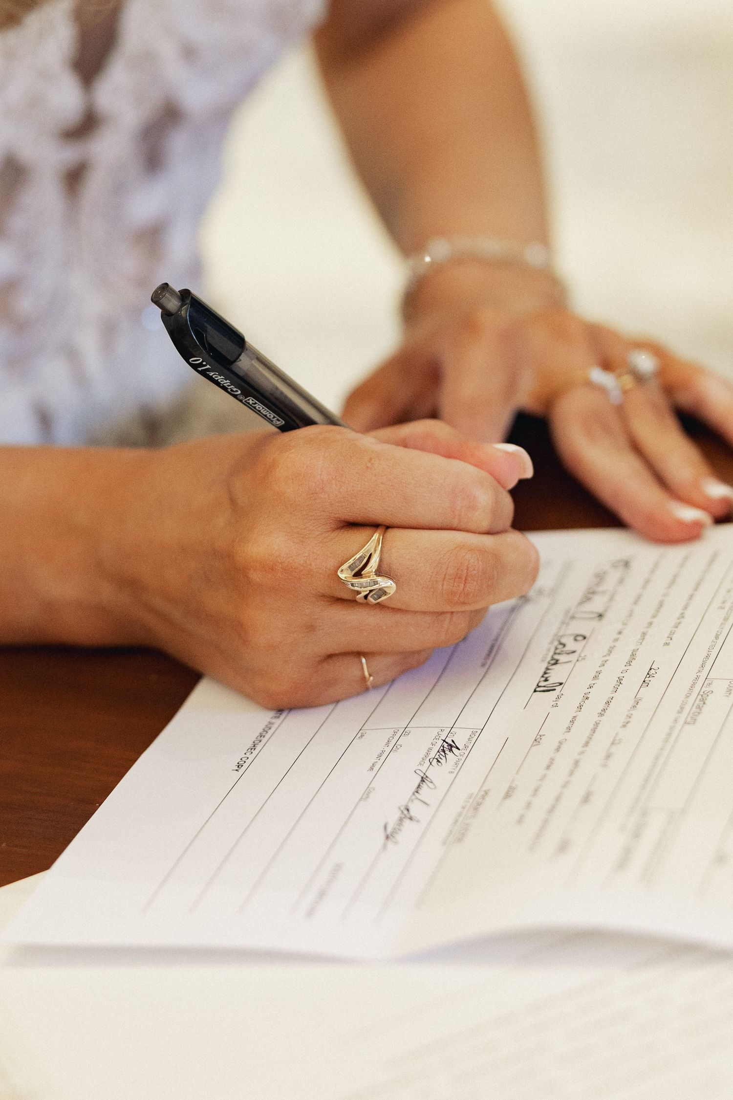 Woman signing a marriage certificate with a pen, wearing a gold ring and bracelet.